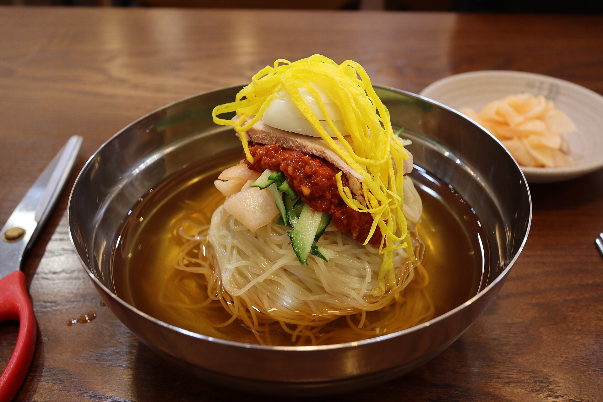 A bowl of Busan milmyeon cold wheat noodles in broth with toppings