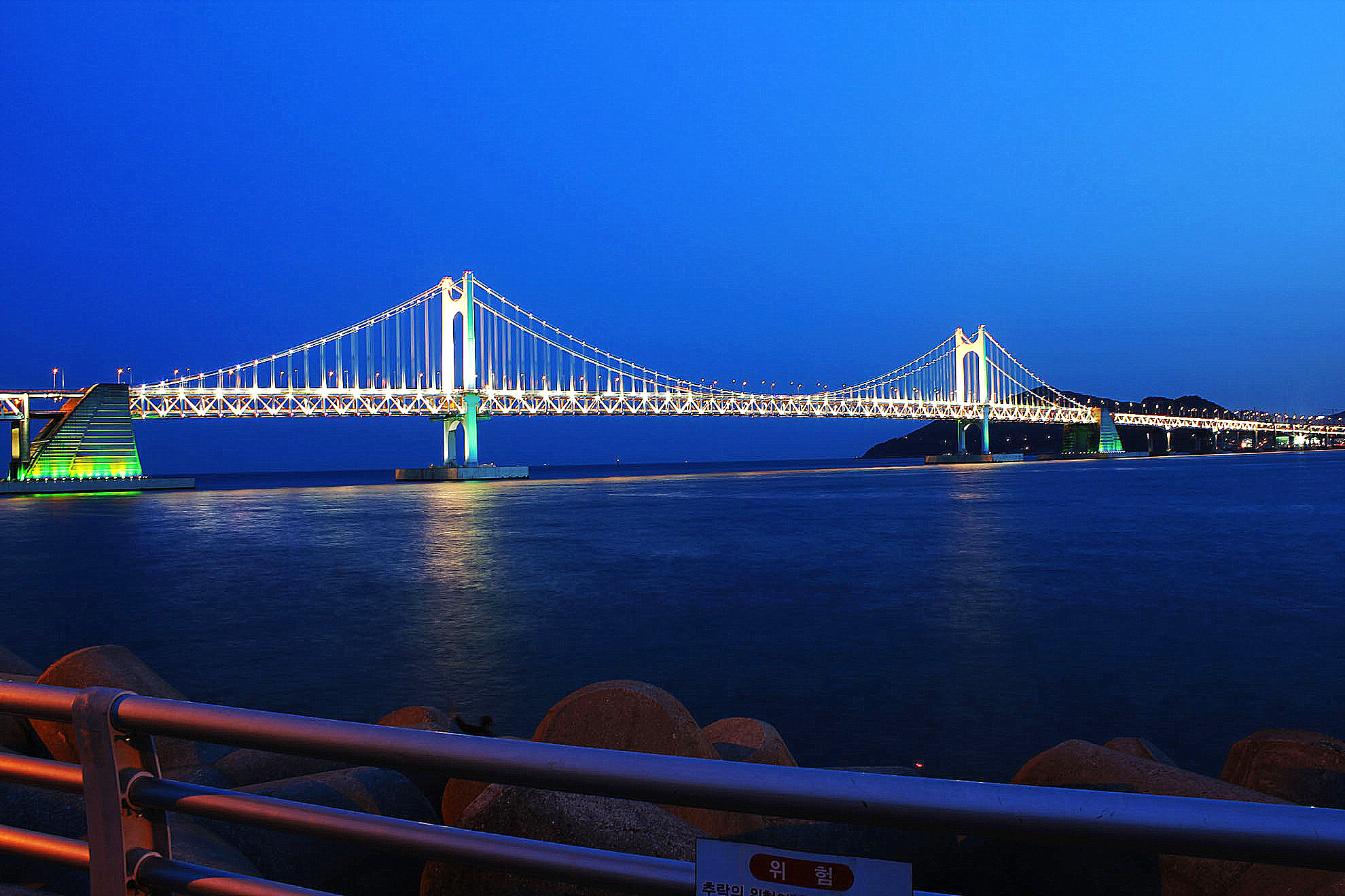 Gwangan Bridge fully lit at night over calm water, seen from the Gwangalli waterfront
