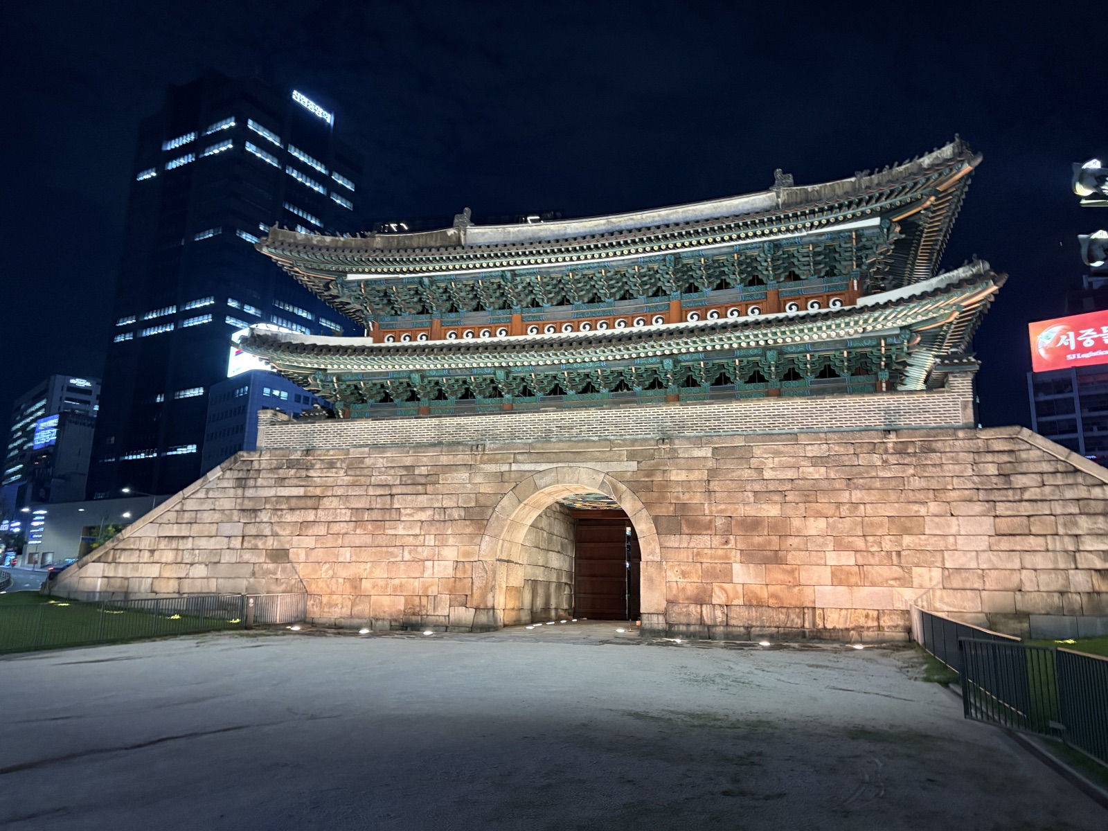 Namdaemun Gate (Sungnyemun) lit up at night in central Seoul, its tiled roof glowing above the old stone base