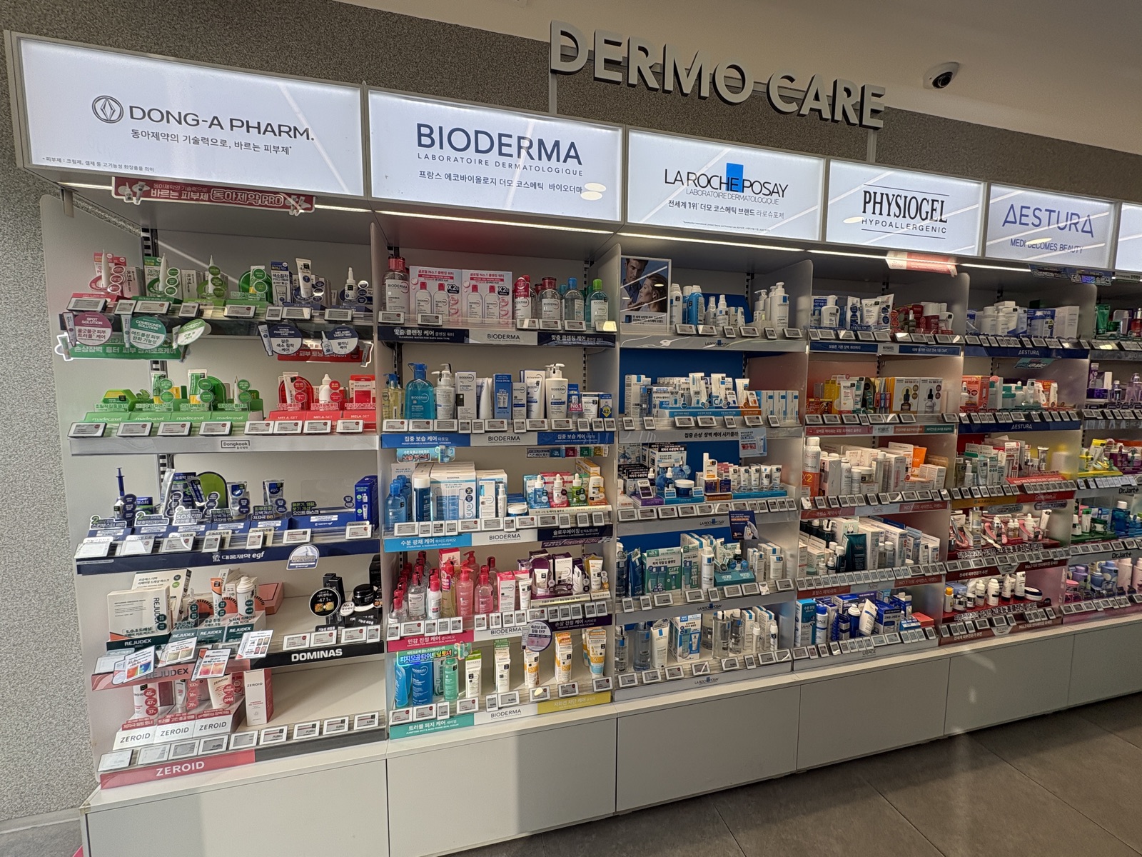 The Dermo-Care skincare wall inside a Korean Olive Young — La Roche-Posay, Bioderma, Physiogel, Aestura and Dong-A Pharm shelves