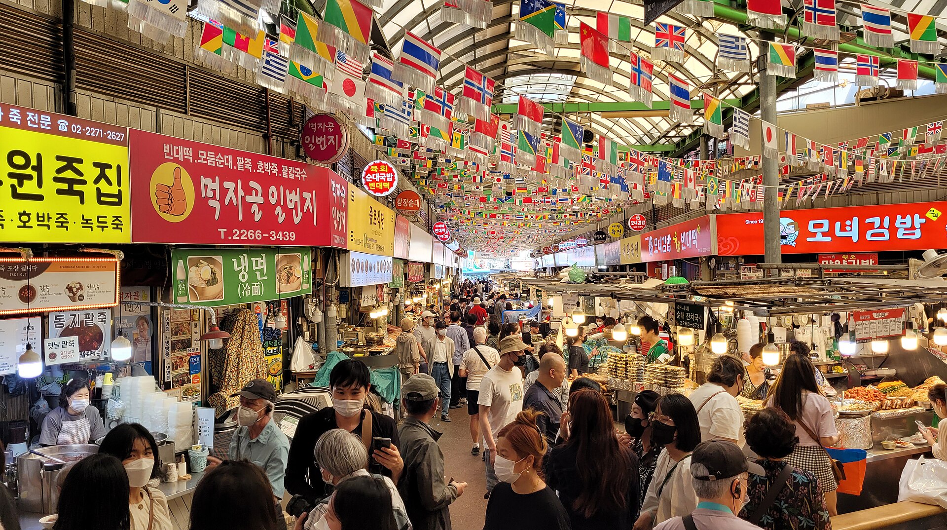 Crowded street-food alley inside Gwangjang Market in Seoul, hung with flags