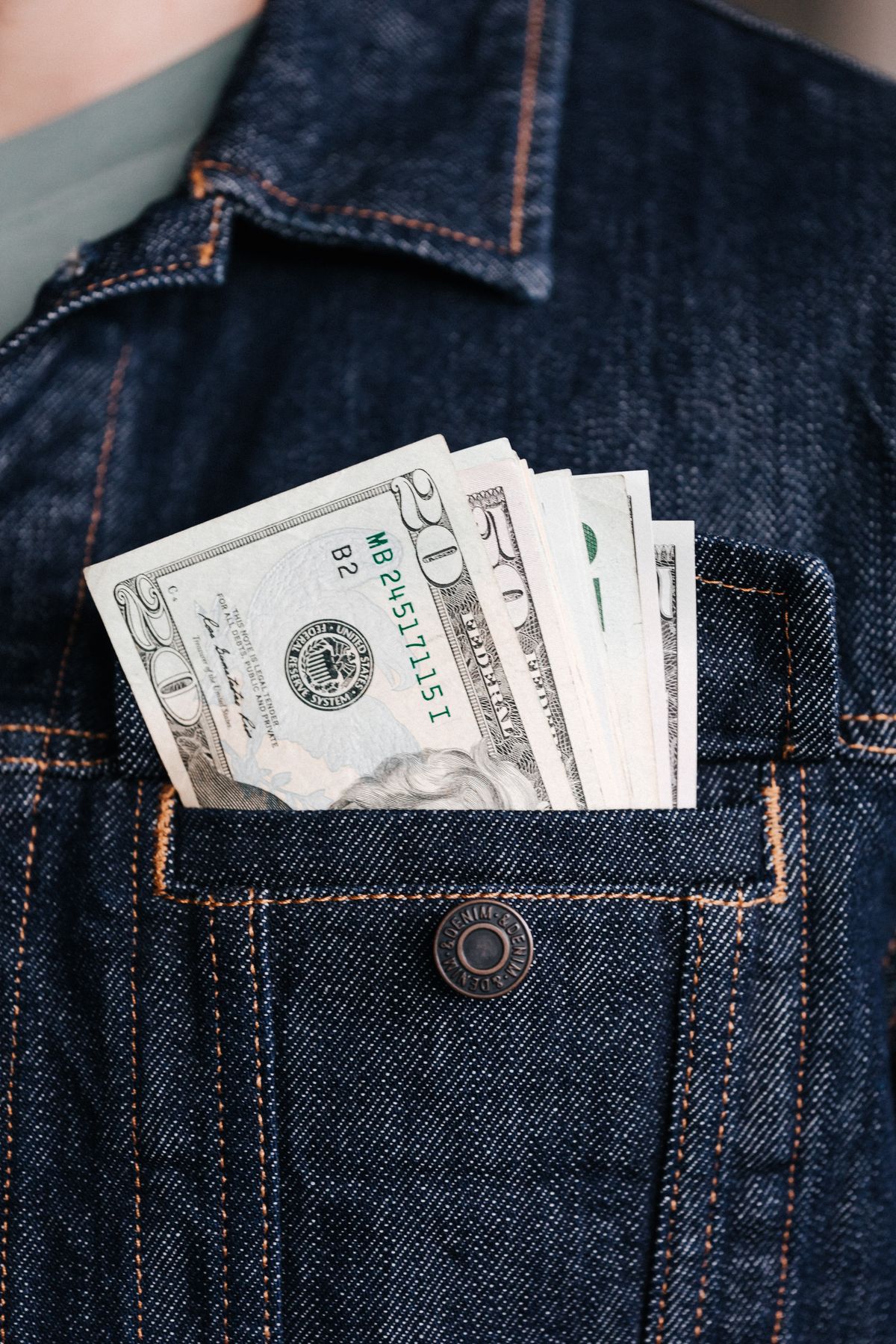 US twenty-dollar bills and other banknotes tucked into the chest pocket of a dark denim jacket.