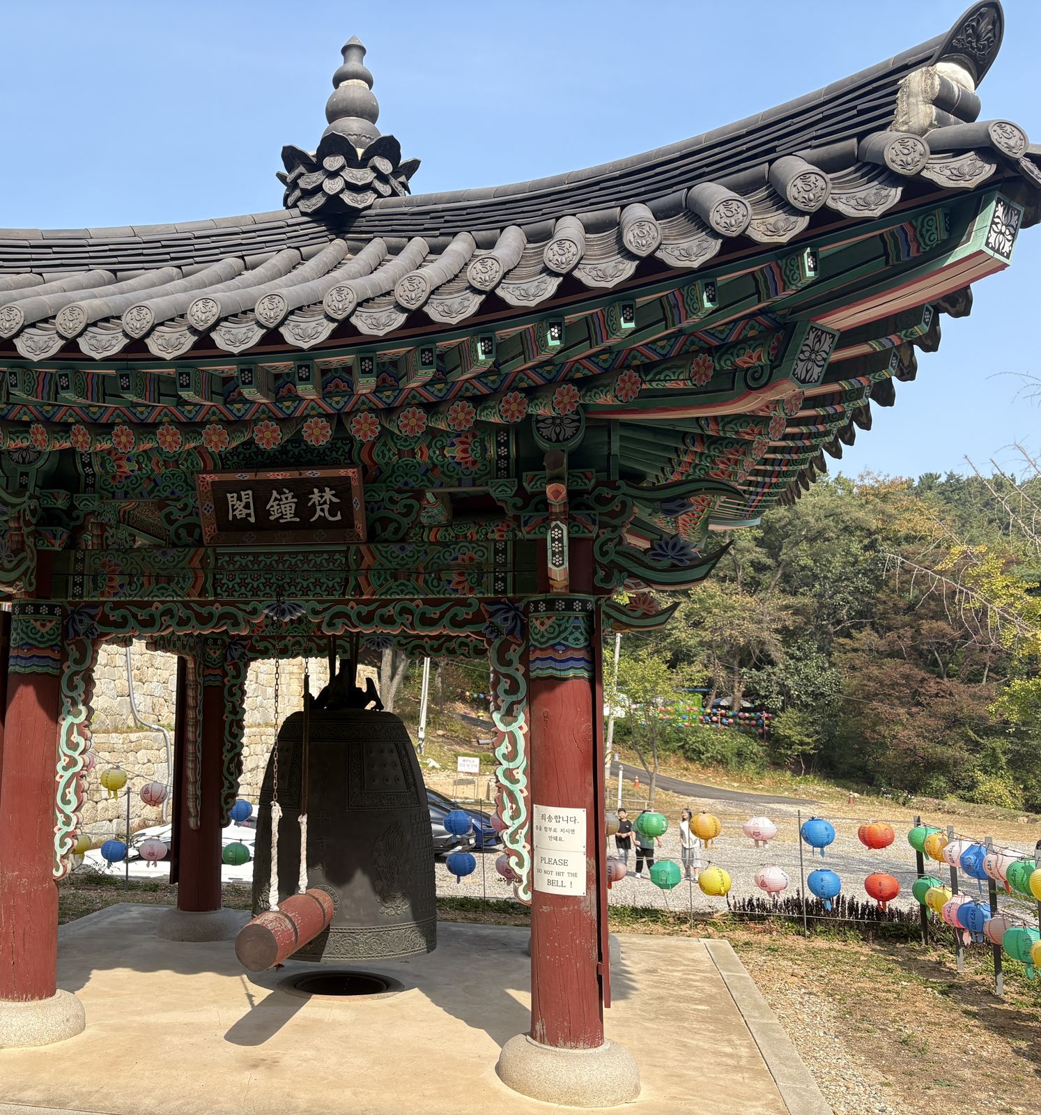 A traditional bell pavilion with a large bronze bell and colorful lanterns behind it
